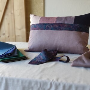 Peut inclure: Un tas d'échantillons de tissu bleu, vert et violet sur une nappe blanche. Un coussin patchwork violet et rose est posé sur la table, ainsi qu'une cravate à motif violet et bleu et un morceau de tissu plié.