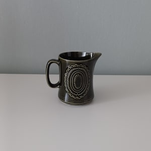 Może przedstawiać: Kremówka ceramiczna w ciemnozielonym kolorze z białym i zielonym wzorem w kształcie koła.