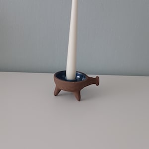 May include: A brown ceramic candle holder with four legs and a blue glazed interior. A white candle is placed in the holder.