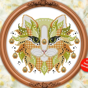 May include: A cross-stitch pattern featuring a stylized cat head in shades of orange, green, and white with a checkered texture. The design includes small pumpkin icons and is framed in a round wooden frame with the text Kitty Me Designs, Colorful Cats, October, and Designed by Pamela Kellogg.