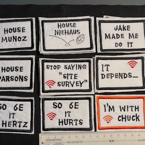 May include: Ten white rectangular patches with black borders and black embroidered text. The patches feature various phrases, including "House Munoz", "House Parsons", "Jake Made Me Do It", "So 6E It Hurts", and "I'm With Chuck".