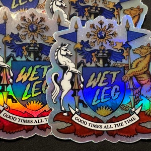 May include: A holographic sticker with a coat of arms design. The crest features a unicorn, a bear, and a shield with the text "WET LEG" and the motto "GOOD TIMES ALL THE TIME".