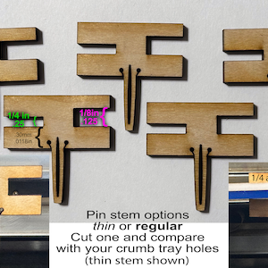 May include: Five wooden crumb tray pin holders with two different stem options: thin or regular. The thin stem is shown in the image. The pin holders are designed to fit 1/4 inch and 1/8 inch holes. The text "Pin stem options thin or regular Cut one and compare with your crumb tray holes (thin stem shown)" is printed below the pin holders.