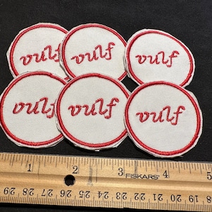 Może przedstawiać: Sześć białych naszywek haftowanych z czerwonymi szwami i napisem "vulf" czerwonymi literami ozdobnymi.