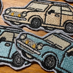 以下が含まれることがあります： ヴィンテージカーの刺繍アイロン接着パッチ3枚。車は青、ベージュ、オレンジ。各車は黒いアウトラインと黒い車輪があります。