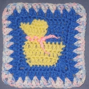 May include: A crocheted square featuring a yellow and pink bear design in the centre. The square is bordered in blue with a pink and white trim.