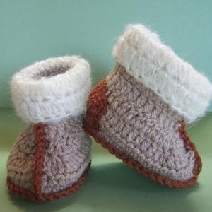 May include: A pair of crocheted baby booties in brown and white. The booties have a white cuff and a brown trim.