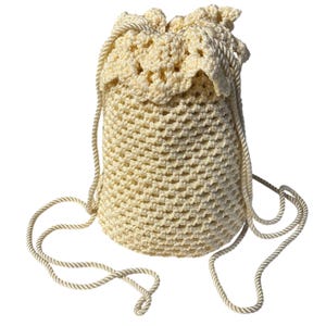 May include: A cream-colored drawstring bag featuring a crocheted net pattern throughout the body. The top edge has a decorative scalloped crochet border. Two long, twisted cream-colored cords serve as both the drawstring closure and shoulder straps.
