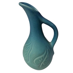 May include: A ceramic pitcher with a matte finish in a gradient of teal and blue. The vessel features a curved handle, a tapered spout, and a rounded body decorated with embossed leaf patterns on the surface, creating a textured appearance.
