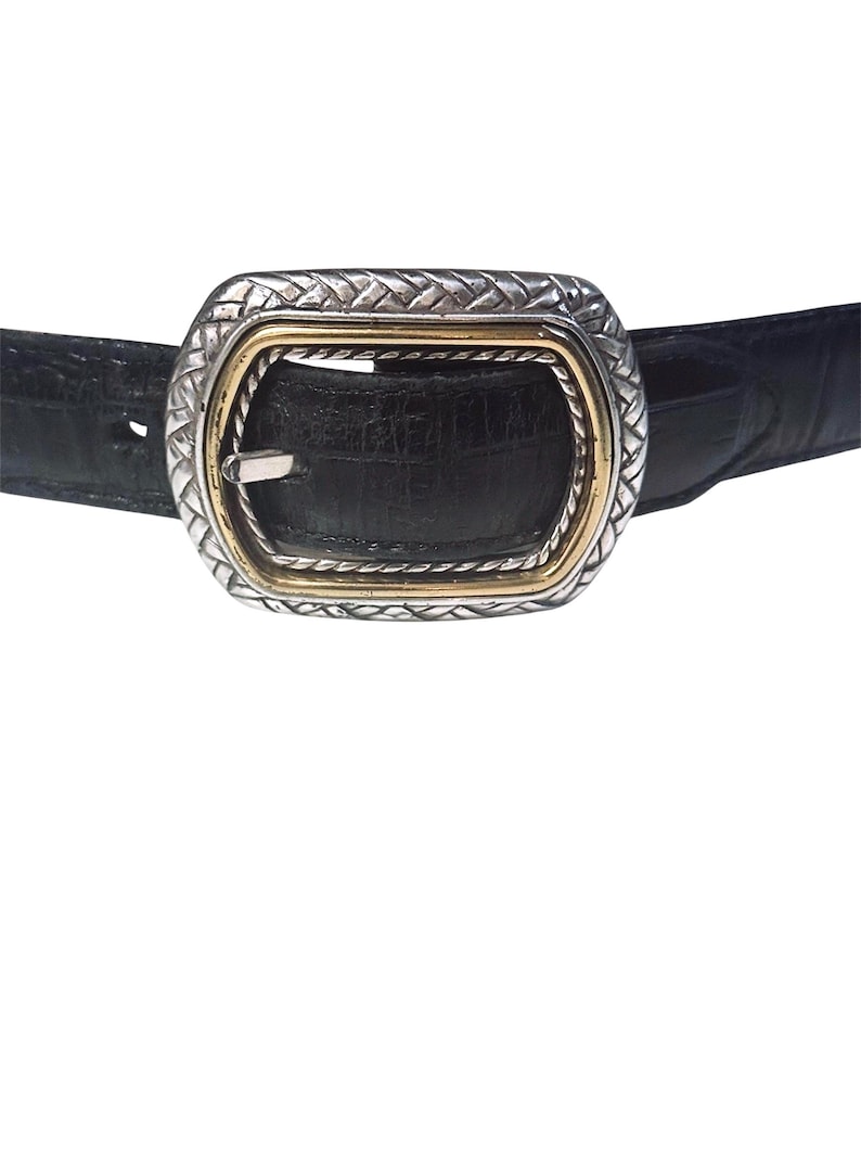 May include: A black belt with a textured crocodile-embossed finish featuring a rectangular buckle. The buckle has a silver-toned outer frame with a woven pattern and a smooth gold-toned inner border surrounding the central prong mechanism.