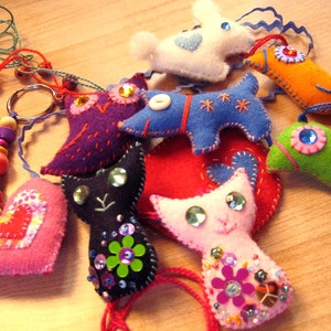 May include: A collection of felt animal keychains, including a cat, a dog, an owl, a heart, a fish, and a bird. The keychains are colorful and feature embroidered details and sparkly embellishments.