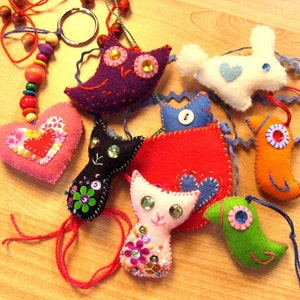 May include: A collection of handmade felt animal ornaments, including a cat, a bird, a rabbit, and a heart. The ornaments are decorated with colorful buttons, beads, and sequins.