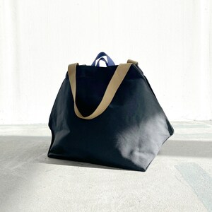 May include: A large black canvas tote bag with tan straps. The bag is sitting on a concrete surface.