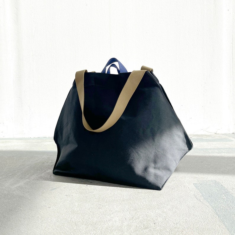 May include: A large black canvas tote bag with tan straps. The bag is sitting on a concrete surface.