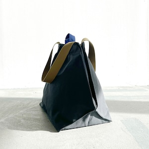 May include: A large, dark grey canvas tote bag with brown leather handles and a blue accent on the top handle.