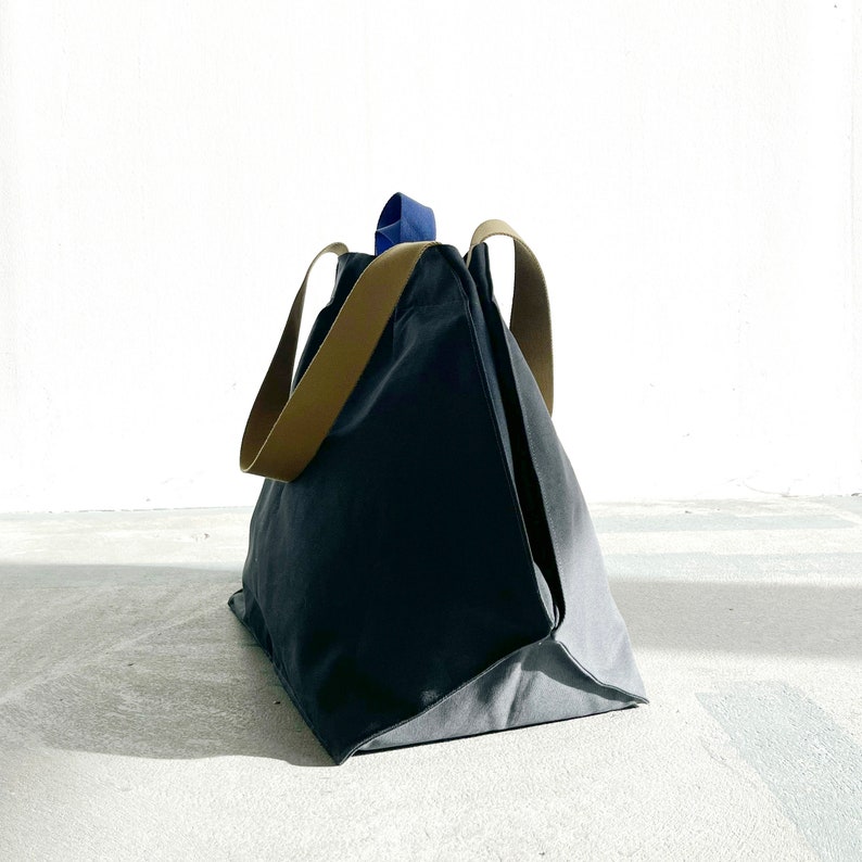 May include: A large, dark grey canvas tote bag with brown leather handles and a blue accent on the top handle.
