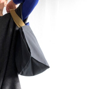 May include: A black tote bag with a tan strap. The bag is folded over at the top and has a rectangular shape.