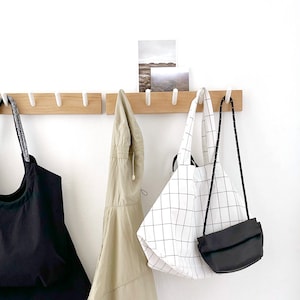 May include: A wooden wall-mounted coat rack with five hooks, holding a black tote bag, a beige jacket, a white and black tote bag, and a black crossbody bag.