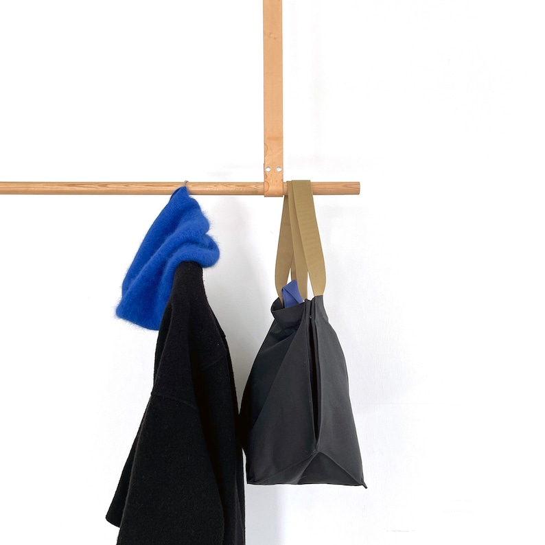 May include: A wooden coat rack with a blue fluffy hat, a black tote bag with brown straps, and a black sweater hanging from it.