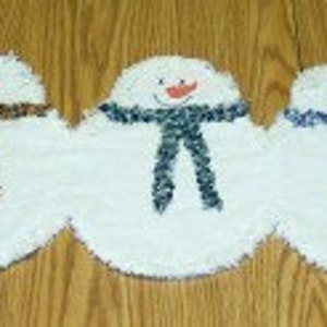 Puede incluir: Cinco alfombras de tela blancas con forma de muñeco de nieve con bufandas de diferentes colores. Las bufandas son burdeos, marrón, azul verdoso, azul y rojo.