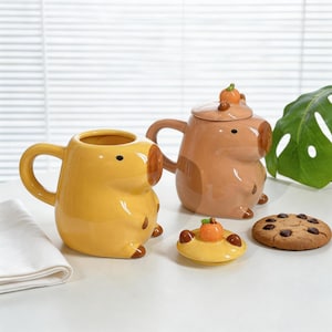 May include: A set of three ceramic mugs with a speckled, matte finish. Each mug features a different color: light blue, cream, and gray. The mugs have a simple, modern design with a rounded shape and a comfortable handle.
