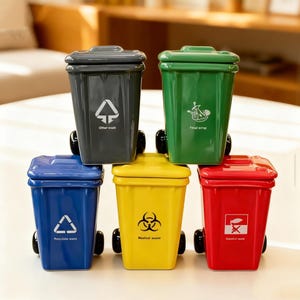 Può includere: Un set di cinque contenitori in ceramica colorati a forma di bidone della spazzatura, con coperchi e ruote. Ogni bidone è di un colore diverso: grigio, verde, blu, giallo e rosso. Ogni bidone ha un simbolo di rifiuto e testo.