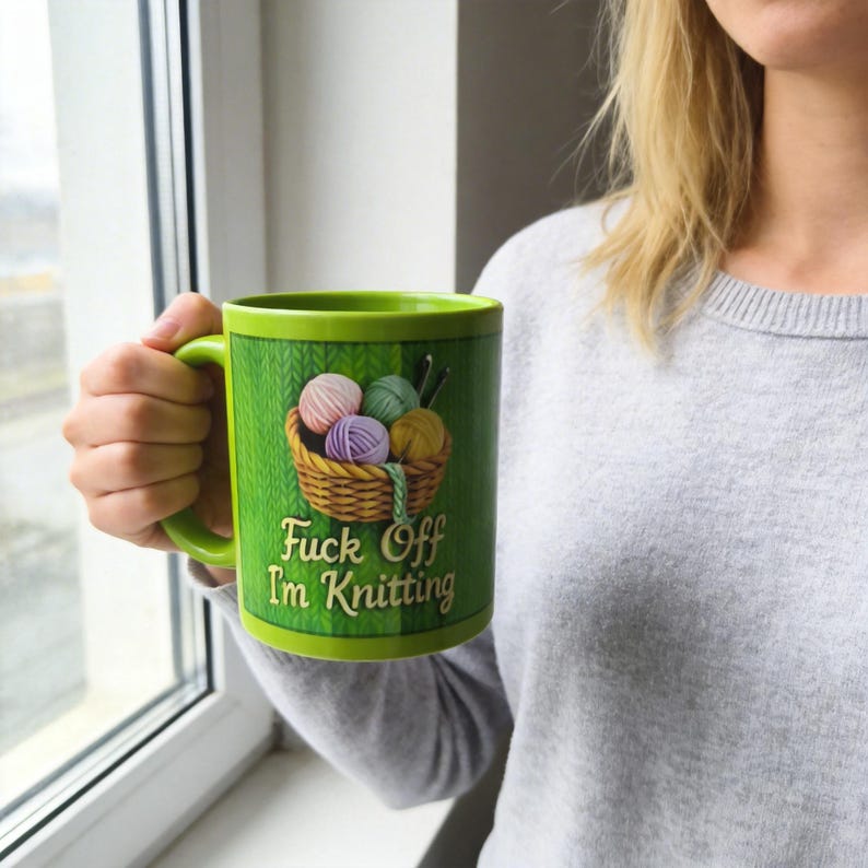 Może przedstawiać: Zielony ceramiczny kubek z koszem kłębk&oacute;w wełny i napisem "Fuck Off I'm Knitting". Kubek ma zielony uchwyt i obramowanie, a tło przedstawia wz&oacute;r dzianiny.