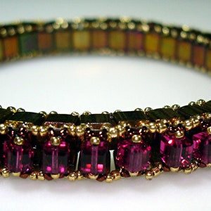 Könnte beinhalten: Ein goldfarbenes und violettes Perlenarmband mit einer Reihe quadratischer violetter Perlen.