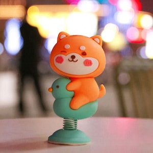 May include: A small orange and white cartoon dog figurine riding a blue and green spring-loaded bird. The figurine is a popular car dashboard decoration.
