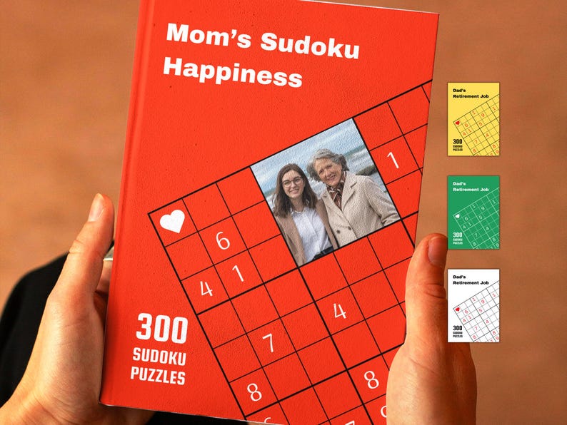 Puede incluir: Un libro rojo con el t&iacute;tulo "Mom's Sudoku Happiness" y una foto de dos personas en la portada. El libro contiene 300 rompecabezas de Sudoku.