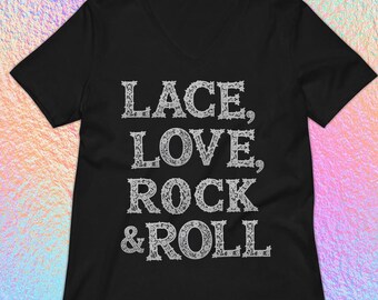 May include: Black V-neck t-shirt with the words "LACE, LOVE, ROCK & ROLL" in a decorative, white font. The shirt has short sleeves and a relaxed fit. The background is a colorful, iridescent gradient.