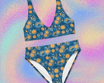 May include: A two-piece bikini set featuring a deep blue background with a repeating pattern of yellow suns, crescent moons, and small stars. The top has a V-neckline and wide straps, while the bottom is a high-waisted style with white lining.