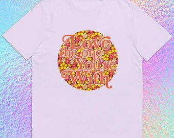 May include: A light pink t-shirt with a round floral design in the center. The design features a mix of yellow, orange, and red flowers, with the words "Love the one You're With" in a retro font.
