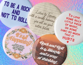 May include: Five circular pin-back buttons featuring various designs. One is light blue with dark blue text reading TO BE A ROCK AND NOT TO ROLL. One has lined paper texture with black text. One is white with red text and a heart. One is pink with floral borders and text. One is brown with white text.