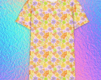 May include: A short-sleeved t-shirt featuring a repeating floral pattern in shades of yellow, orange, light green, and purple against a pale pink background. The garment has a crew neckline and a straight hemline, showcasing a consistent print.
