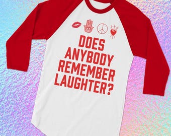 May include: A white and red baseball tee with the text "DOES ANYBODY REMEMBER LAUGHTER?" in red. The shirt features red sleeves and a white body. Above the text are red graphics of a kiss, a hand, a peace sign, and a heart.