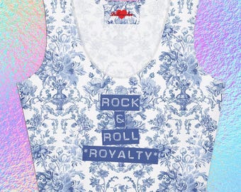 May include: A white crop top with a blue floral pattern and the words "ROCK & ROLL ROYALTY" in a blue rectangular box. The top has a scoop neck and is sleeveless. A small label with a heart is visible.