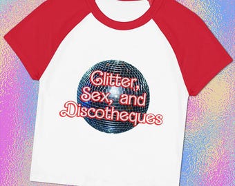 May include: A white raglan t-shirt with short red sleeves and a red collar. The center of the shirt features a graphic of a silver disco ball with the red text "Glitter, Sex, and Discotheques" layered over the center of the sphere.