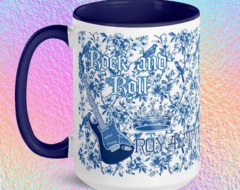 May include: White ceramic mug with a navy blue handle and interior. The mug features a blue floral pattern with a guitar, crown, and the words "Rock and Roll Royalty" in a decorative font.