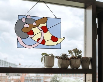 May include: A stained glass window hanging in a window frame. The stained glass depicts a rat holding a slice of pizza. The pizza is yellow with red pepperoni. There are potted plants on a shelf below the window.
