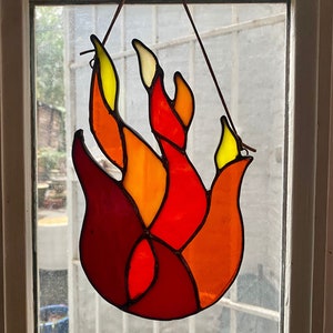 May include: A stained glass window hanging with a flame design. The flame is made of red, orange, and yellow glass pieces.