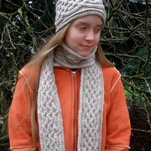 Peut inclure: Une femme portant un bonnet et une écharpe en tricot gris. Le bonnet et l'écharpe ont un motif en tricot torsadé. La femme porte une veste orange vif.
