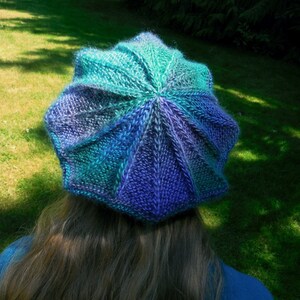 Puede incluir: Un gorro de punto con un esquema de color azul, morado y verde. El gorro está hecho con un patrón de punto texturizado y tiene una corona redondeada.