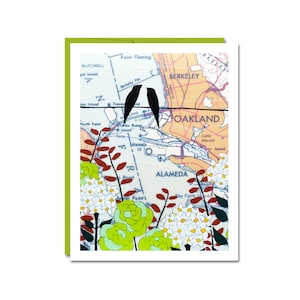 May include: A vintage map of Oakland, California with a pair of black birds perched on a wire. The map is surrounded by white and green flowers with red stems.