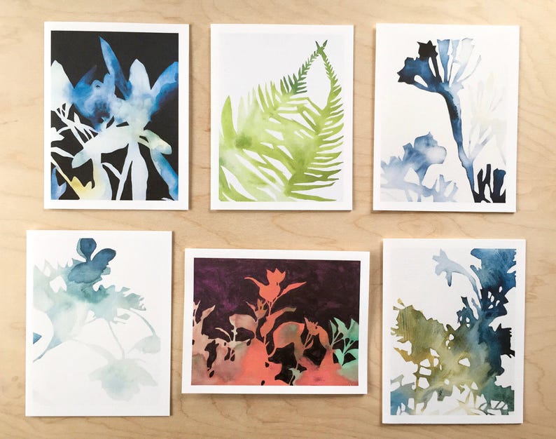 K&ouml;nnte beinhalten: Satz von sechs Aquarell-Gru&szlig;karten mit verschiedenen botanischen Illustrationen. Die Karten sind wei&szlig; mit schwarzem Rand und zeigen blaue, gr&uuml;ne und orangefarbene Aquarell-Illustrationen von Bl&auml;ttern und Blumen.