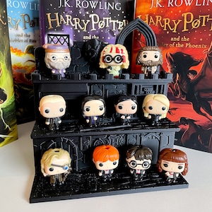 Könnte beinhalten: Ein schwarzer Präsentationsständer mit 10 Harry-Potter-Charakterfiguren. Der Ständer hat drei Ebenen und ist im Hogwarts-Schloss-Design gehalten. Die Figuren umfassen Harry Potter, Ron Weasley, Hermine Granger, Draco Malfoy, Severus Snape, Albus Dumbledore, Luna Lovegood, Neville Longbottom, Ginny Weasley und Cho Chang.
