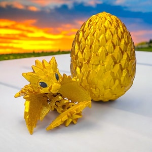 Könnte beinhalten: Eine goldene Drachenfigur mit ausgebreiteten Flügeln, die auf einem goldenen, eiförmigen Behälter sitzt. Der Drache hat schwarze Augen und ein detailliertes Design.