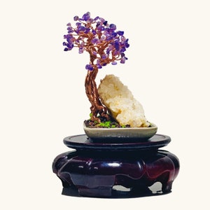 May include: A purple amethyst wire wrapped tree with a white crystal rock base, sitting on a dark wood stand.