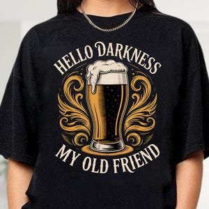 A black t-shirt with a graphic design featuring a beer glass and the text "HELLO DARKNESS MY OLD FRIEND" printed on it.
