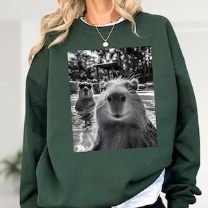 A woman wearing a green sweatshirt with a printed image of two beavers swimming in a pool.
